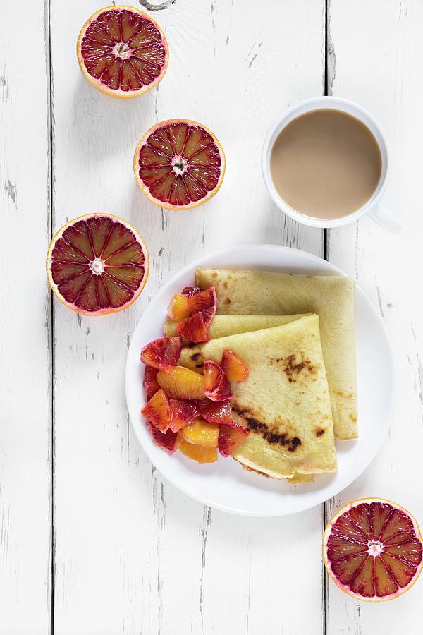 Crepes With Blood Oranges On A Plate With A Cup Of Coffee And Halved Blood Oranges Next To It Photograph by Malgorzata Laniak