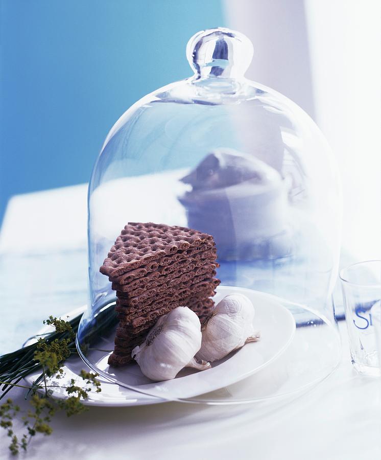Crisp Breads And Garlic Under A Decorative Glass Cloche Photograph by Matteo Manduzio