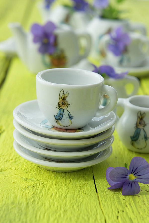 Crockery With Peter Rabbit Motif And Violas On Yellow-painted Wooden Table Photograph by Martina Schindler