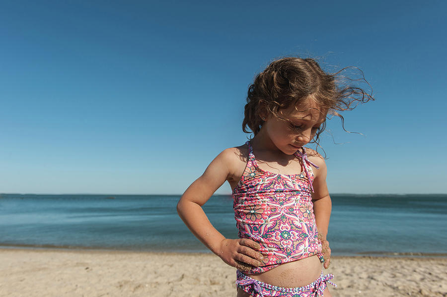 Cute Girl Standing With Hands On Hip At Beach Against Sky Photograph by ...