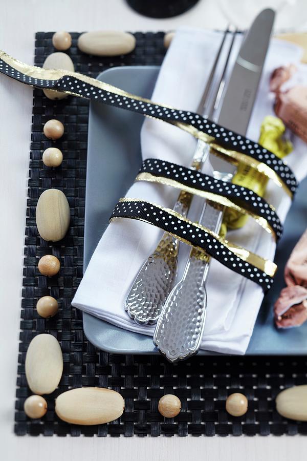 Cutlery And Napkin Tied With Black And Gold Ribbon On Place Mat With Wooden Beads Photograph by Franziska Taube