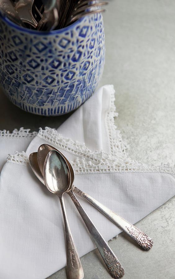 Cutlery Holder With A Blue And White Design; To One Side, A Lace-edged Napkin And Three Antique Silver Spoons Photograph by Campbell, Ryla