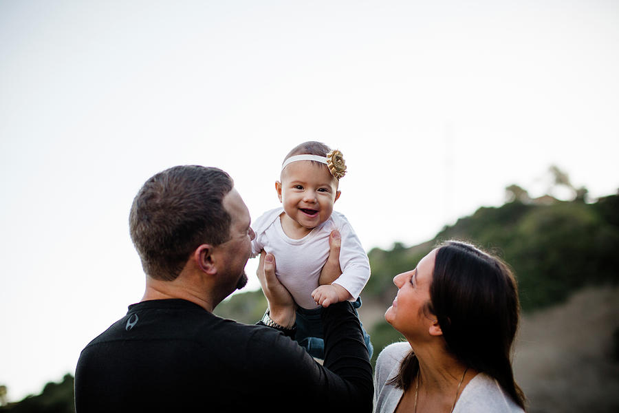 Fall Photograph - Dad Lifting Infant Daughter As Baby Laughs & Mom Watches by Cavan Images