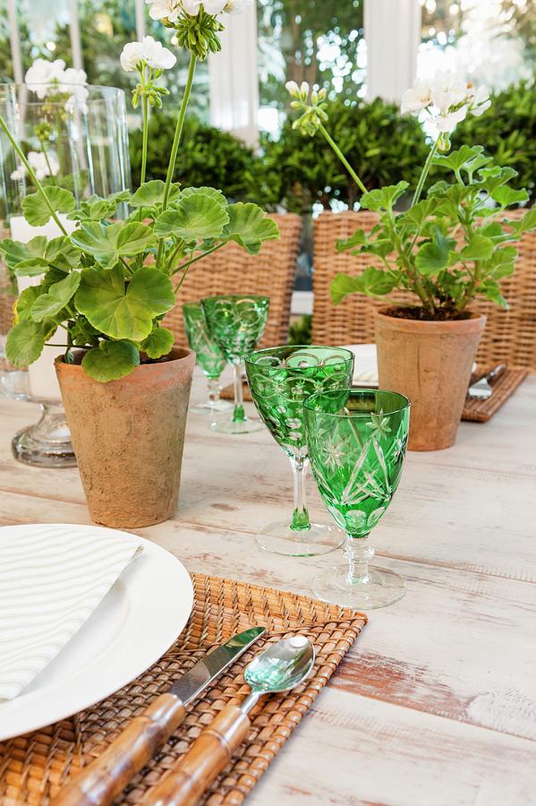 Detail Of Table Set With Green Crystal Glasses, Woven Place Mats And Potted Geraniums Photograph by Great Stock!