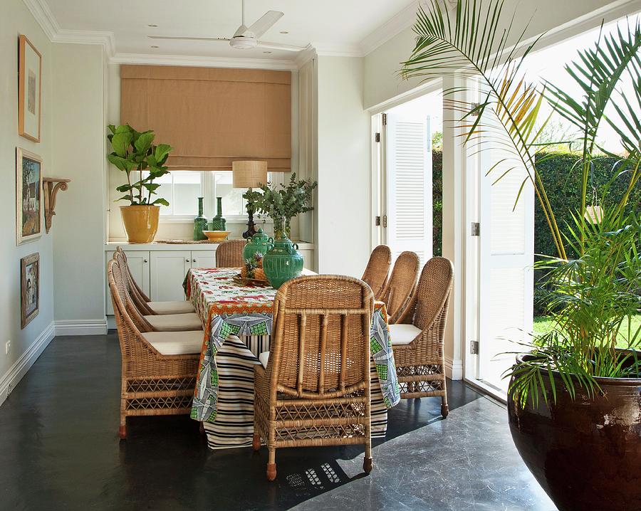 Dining Area With Wicker Chairs And Table In Front Of Open Shutters On Terrace Doors Leading To Garden Photograph by Great Stock!