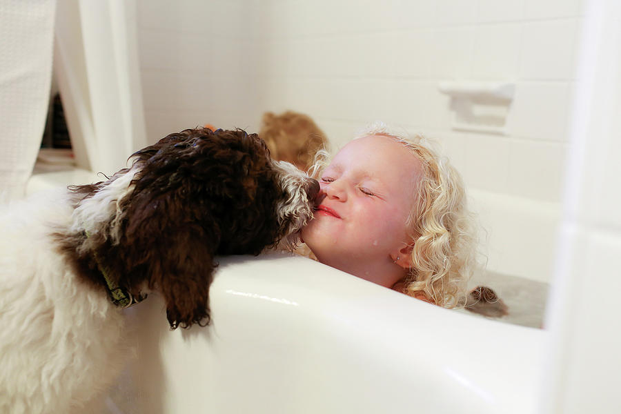 Dog Photograph - Dog Kissing Girl Sitting In Bathtub In Bathroom by Cavan Images