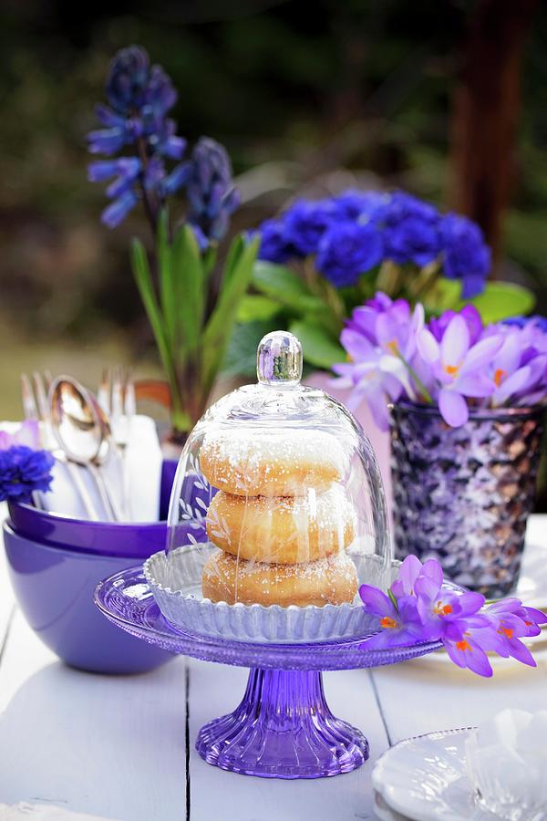 Doughnuts Under A Glass Cloche On A Table Outside Decorated With Crockery And Blue And Purple Flowers Photograph by Angelica Linnhoff