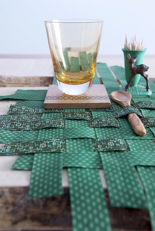Drinking Glass, Wooden Accessories And Fawn Figurine On Placemat Made From Green Patterned Strips Of Fabric Photograph by Matteo Manduzio
