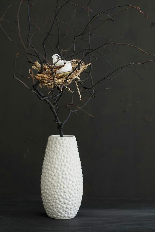 Easter Arrangement Of Birds Nest Amongst Black Branches In White Vase Against Black Wall Photograph by Ulla@patsy