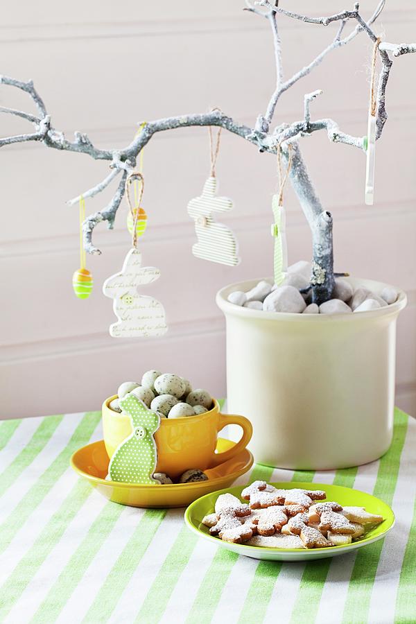Easter Arrangement With Rabbits And Eggs Hanging From Branch Above Cup Of Quails Eggs And Plate Of Easter Biscuits Photograph by Uwe Merkel