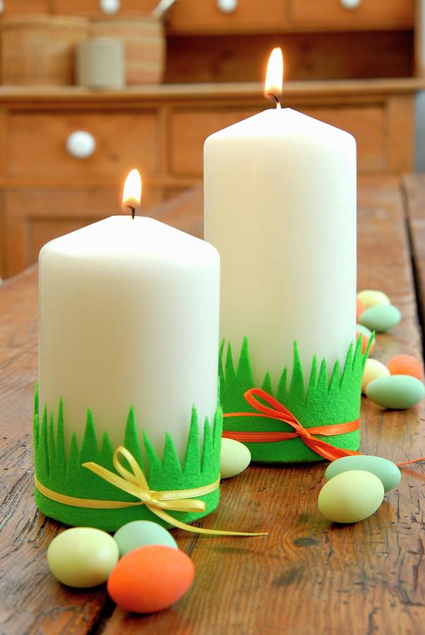 Easter Decorations - Pillar Candles Decorated With Strips Of Felt On Rustic Wooden Table Photograph by Thordis Rggeberg