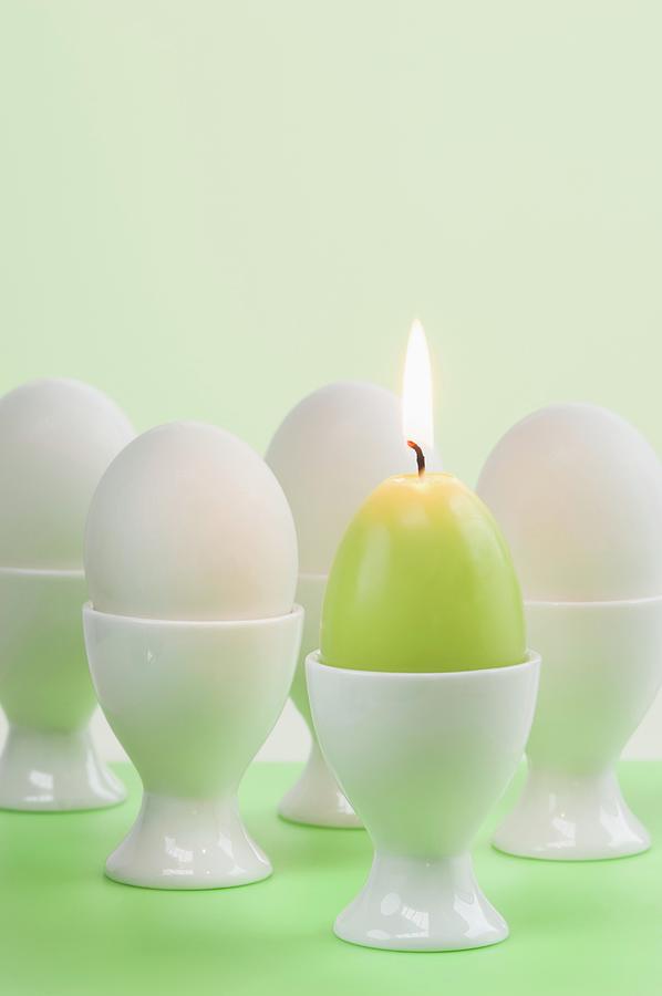 Easter Eggs And Egg-shaped Candle In Egg Cups Photograph by Achim Sass
