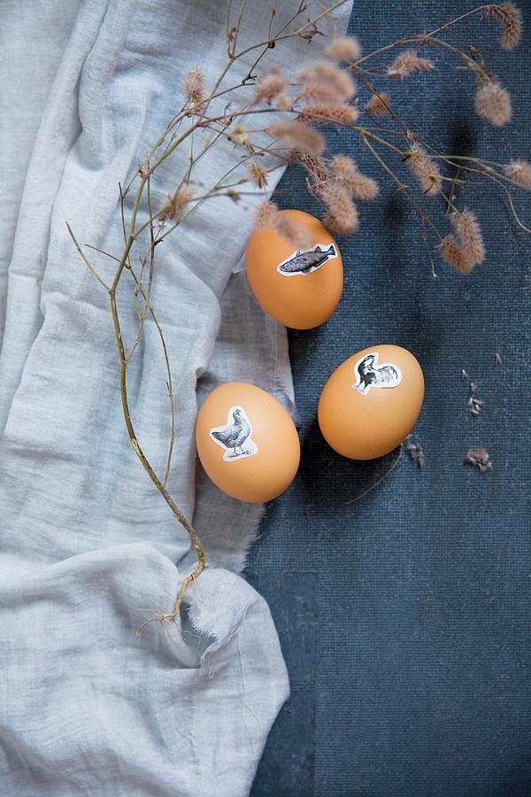 Easter Eggs Decorated With Animal Stickers And Dried Twig On Blue Fabric Photograph by Alicja Koll