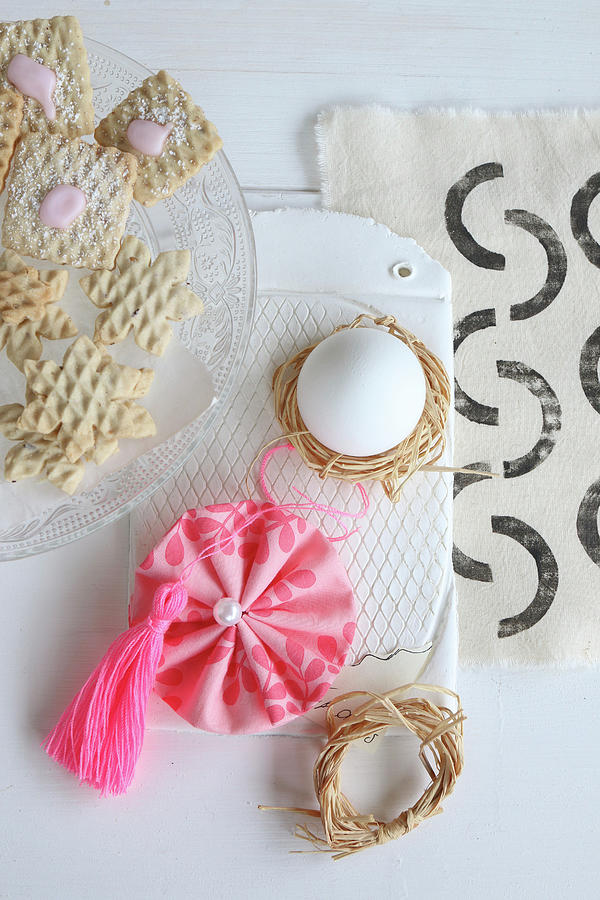 Egg In Raffia Nest, Fabric Rosette And Pink Tassel Next To Plate Of Biscuits Photograph by Regina Hippel
