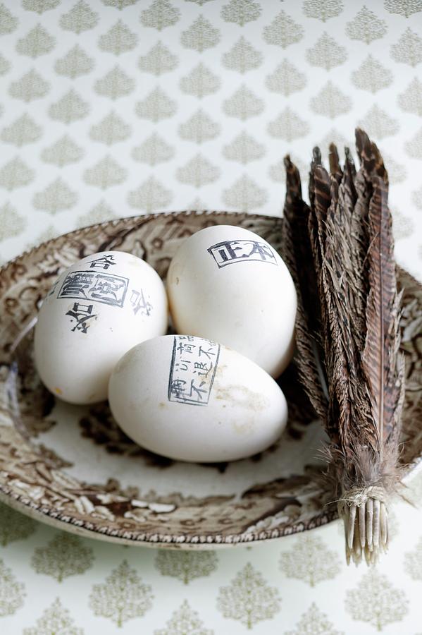 Eggs Stamped With Lettering Next To Bundle Of Feathers On Plate Photograph by Bjarni B. Jacobsen