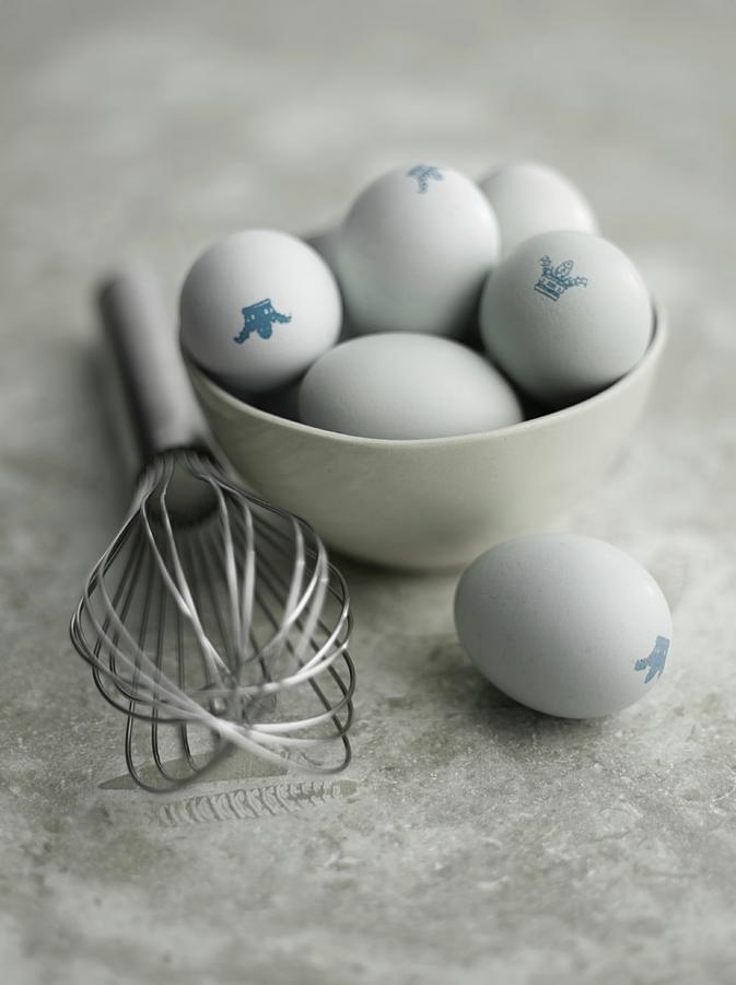 Eggs With A Crown Stamp In A Bowl Next To An Egg Whisk Photograph by Adrian Lawrence