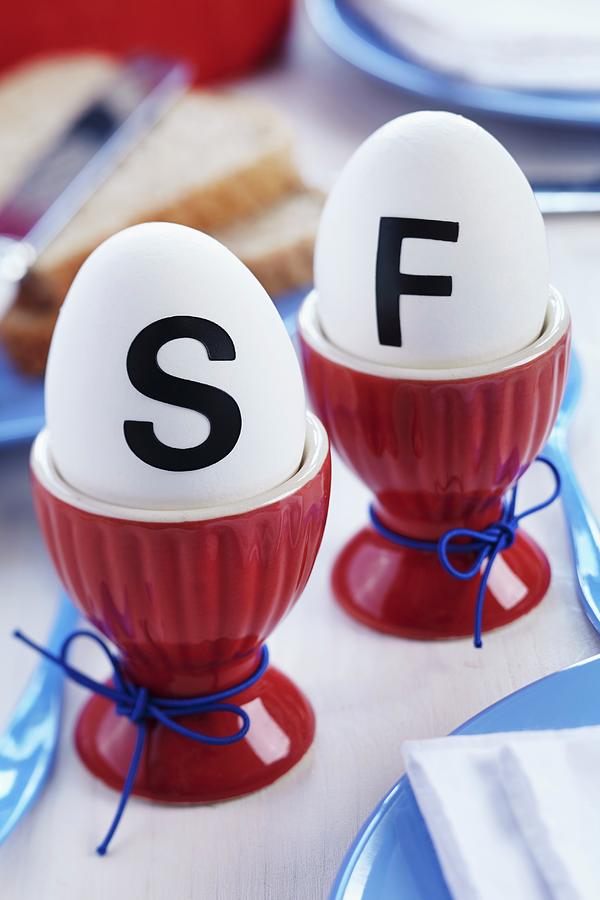 Eggs With Stick-on Initials In Red Eggcups On Breakfast Table Photograph by Franziska Taube