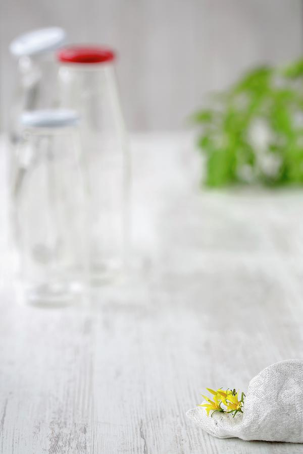 Empty Glass Bottles, Tomato Leaves And A Kitchen Cloth On A Wooden Surface Photograph by Sandra Krimshandl-tauscher
