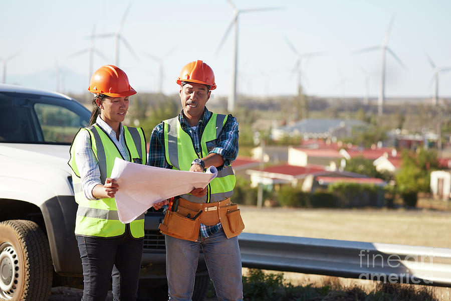 Engineers Reviewing Blueprints Near Wind Turbine Farm Photograph by
