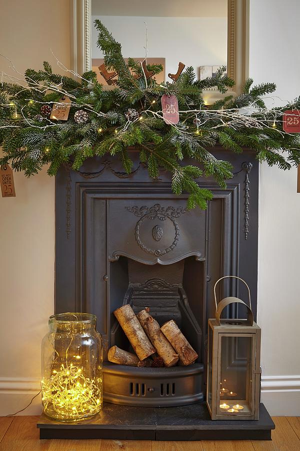 Fairy Lights In Large Glass Jar And Lantern On Hearth Of Cast Iron Fireplace With Festive Arrangement On Mantelpiece Photograph by Tim Imri