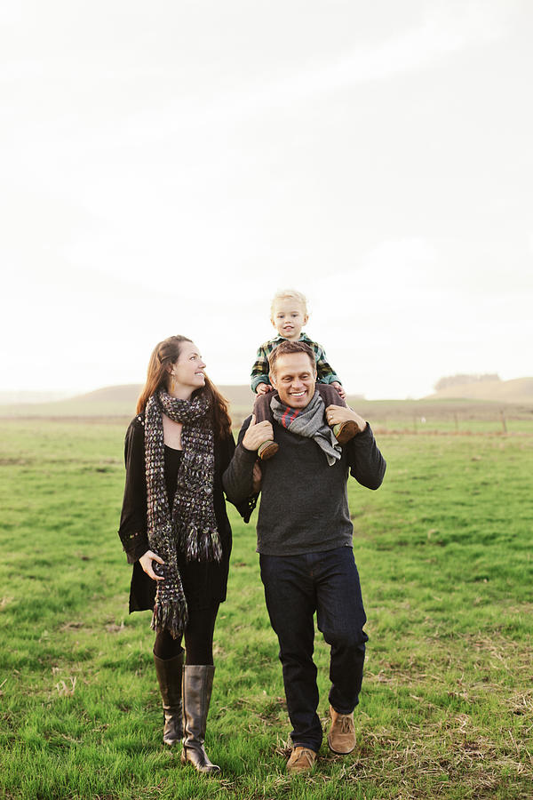 Father Carrying Son On Shoulders While Walking With Wife On Grassy ...