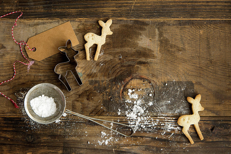 Festive Christmas Deer Shaped Biscuits On A Rustic Board With Cookie Cutter, Icing Sugar In Sifter And Gift Label Photograph by Stacy Grant
