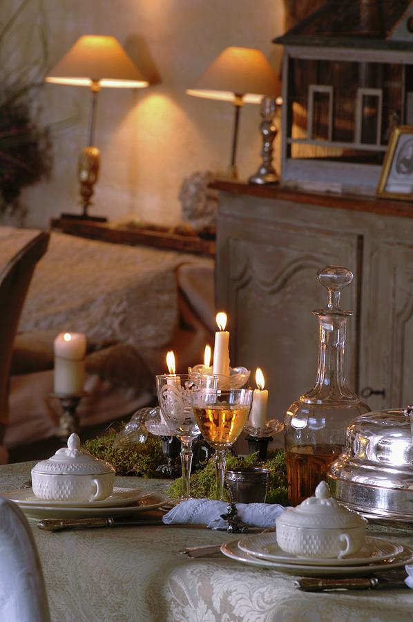 Festively Set Table In Candlelight Atmosphere And Table Lamps On Shelf In Background Photograph by Christophe Madamour