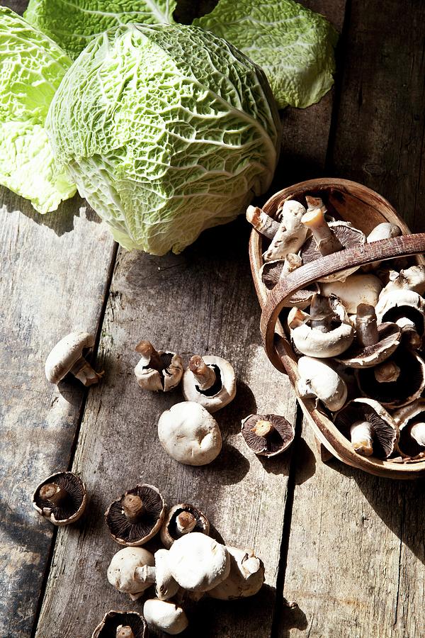 Field Mushrooms On A Wooden Table And In A Wooden Basket Next To Organic Savoy Cabbage Photograph by George Blomfield