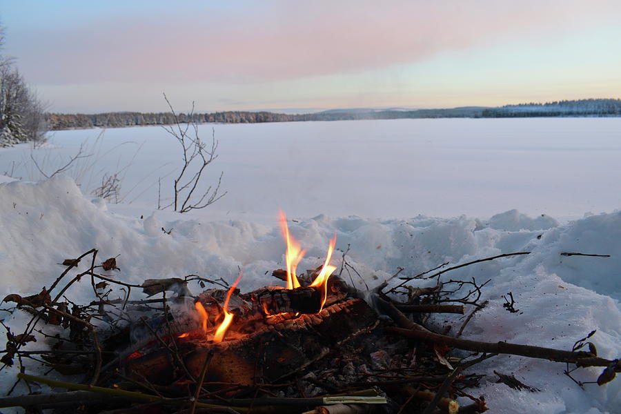 Fire burning in the snow at the shore of a lake at sunset Photograph by Intensivelight