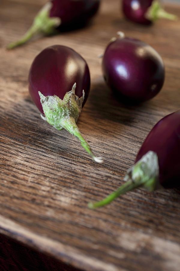 Five Fresh Purple Aubergines On A Wooden Surface Photograph by Katharine Pollak