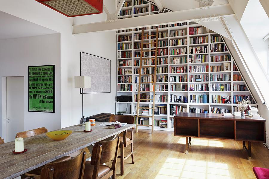 Floor-to-ceiling Bookcase With Wooden Library Ladder Under Sloping Ceiling; Long Wooden Table And Upholstered Chairs In Foreground Photograph by Simon Maxwell Photography