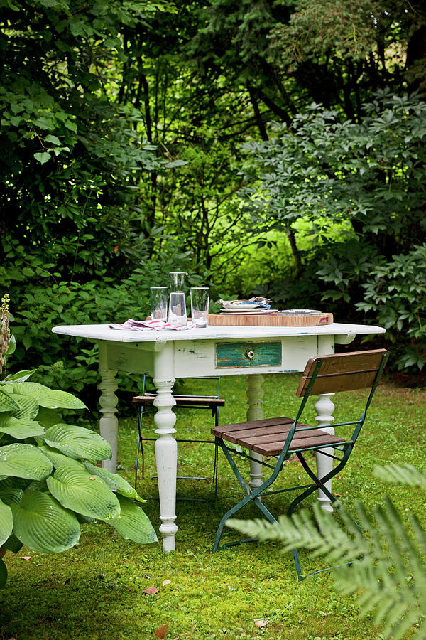 Folding Garden Chair And White-painted, Shabby-chic Table With Turned Legs In Garden Photograph by Sabine Lscher
