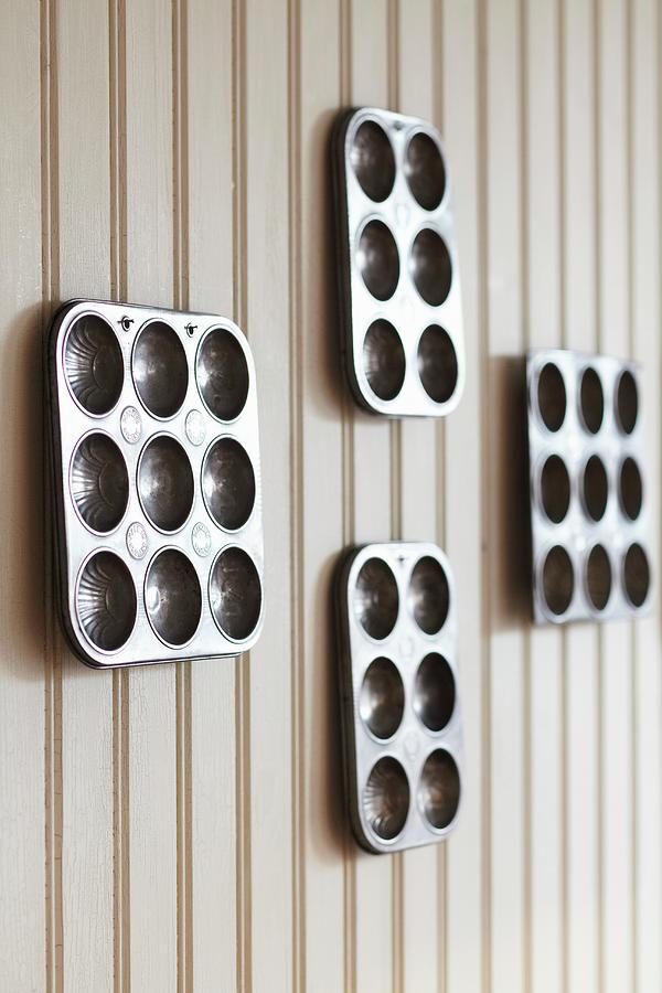 Four Metal Muffin Trays Of Various Sizes On Light Brown Wooden Wall Photograph by Charlotte Tolhurst