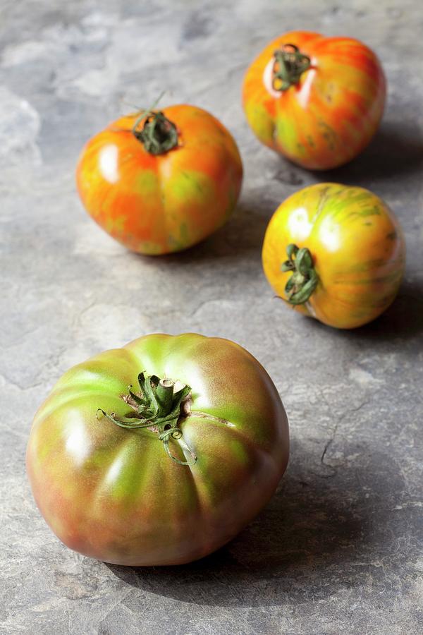 Four Organic Tomatoes On A Stone Surface Photograph by Hilde Mche