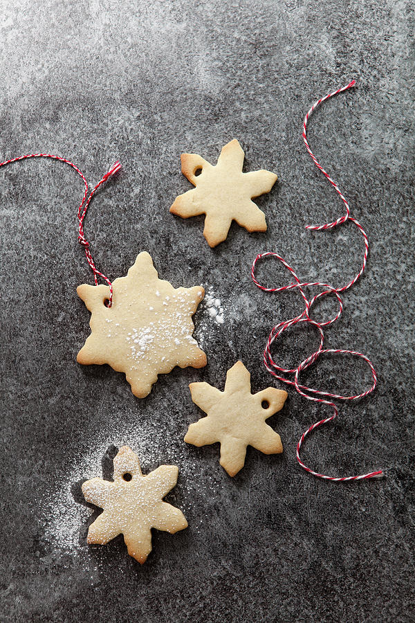 Four Snowflake Shaped Biscuits With A Sprinkling Of Icing Sugar In The Process Of Being Threaded With Red And White Bakers Twine On A Grey Slate Background Photograph by Stacy Grant