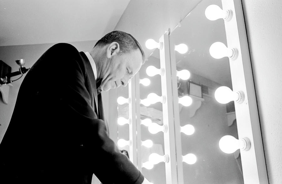 Frank Sinatra standing in front of a mirror sorting through music and notes in his dressing room at a performance. Photograph by John Dominis