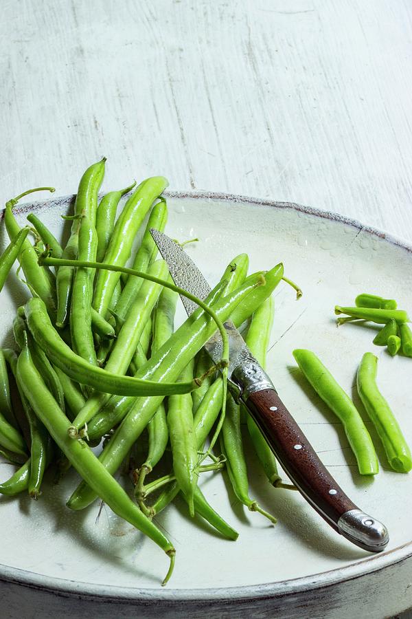 Fresh Beans On A White Plate With A Knife Being Prepared Photograph by Charlotte Von Elm