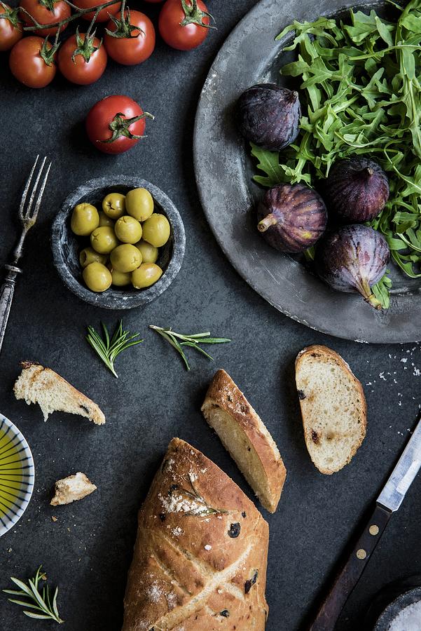 Fresh Bread, Olives, Tomatoes, Lettuce, Figs And Olive Oil On A Grey Table Photograph by Magdalena Hendey