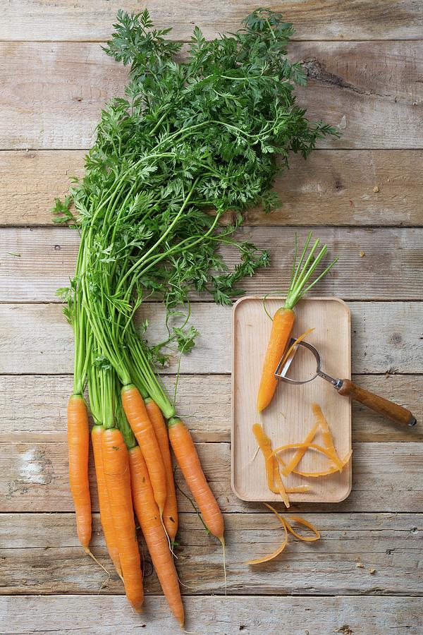 Fresh Carrots Next To A Carrot On A Chopping Board With A Vegetable Peeler Photograph by Claudia Castaldi