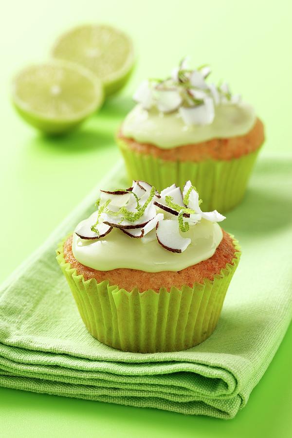 Fresh Coconut And Lime Iced Cupcakes On A Green Napkin And Green Background With 2 Half Limes Photograph by Stuart Macgregor