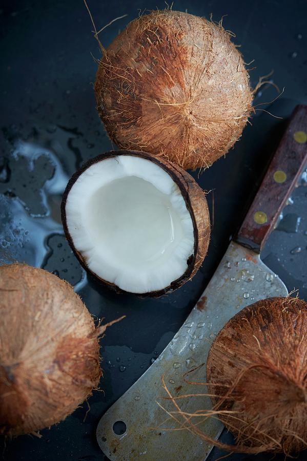 Fresh Coconuts With A Large Knife; One Cracked Open With Spilled Coconut Milk Photograph by Rannells, Greg