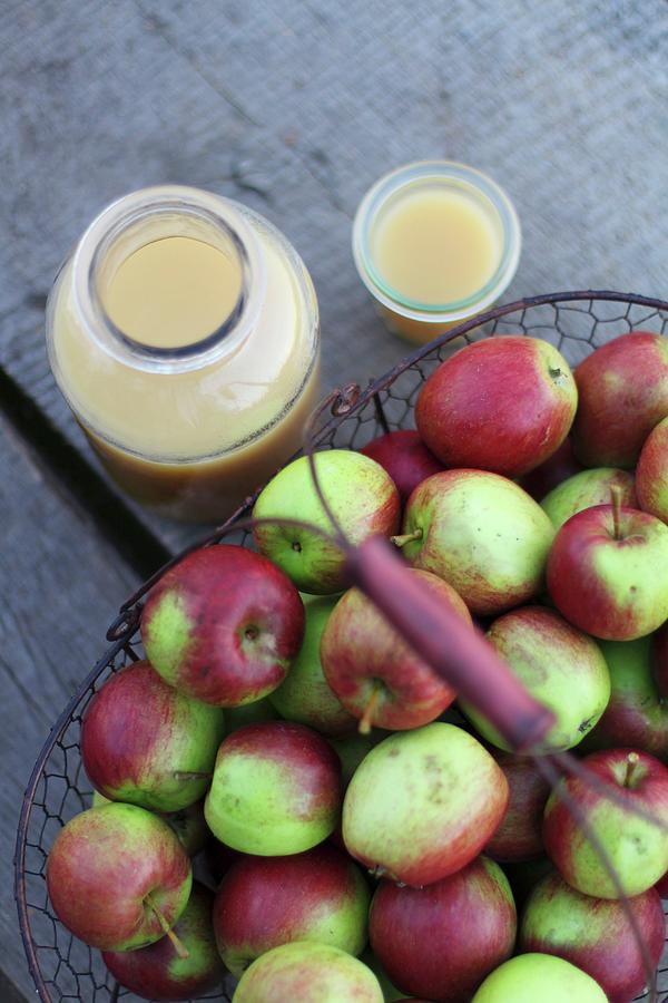 Fresh Naturally Cloudy Apple Juice In A Glass And Bottlenecks To A Basket Of Apples Photograph by Sylvia E.k Photography