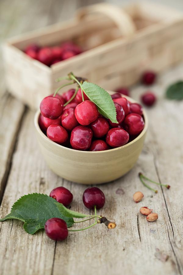 Freshly Harvested Cherries In A Bowl And On A Wooden Table Photograph by Jan Wischnewski
