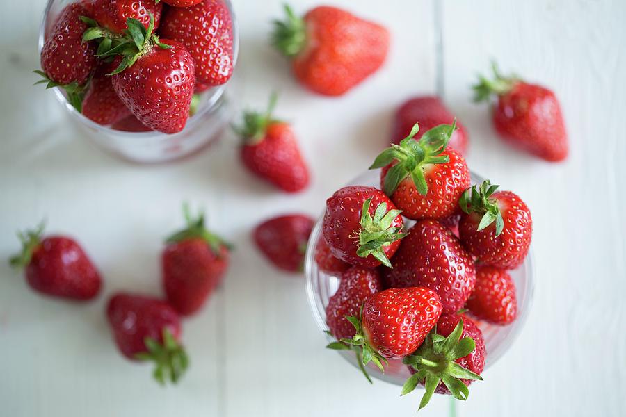 Freshly Washed Strawberries In Glasses On A White Wooden Surface Photograph by Nicole Godt