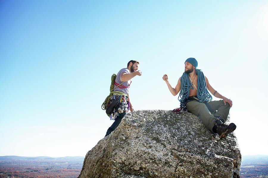 Nature Photograph - Friends Doing Fist Bump While Sitting On Rock Against Clear Sky by Cavan Images