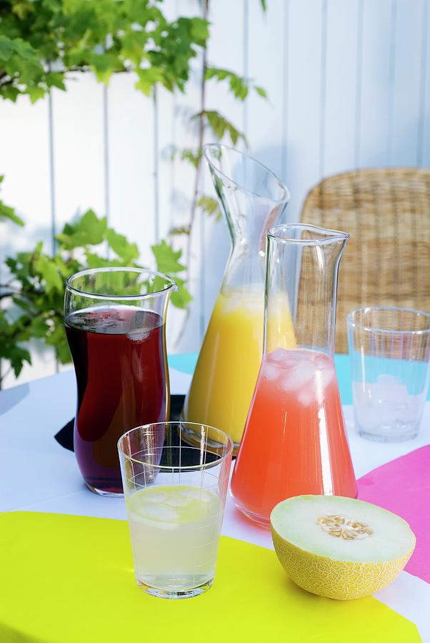 Cube Photograph - Fruit Juice Drinks Cooled With Ice Cubes In Glass Decanters On Summery Garden Table Set With Bright Colours by Matteo Manduzio