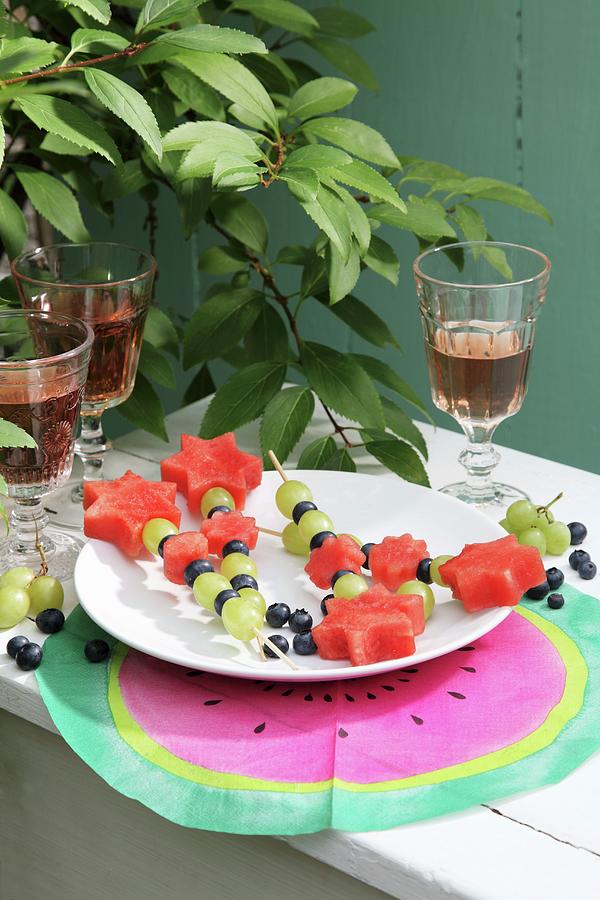 Fruit Skewers On White Plate And Hand-made Place Mat Photograph by Thordis Rggeberg