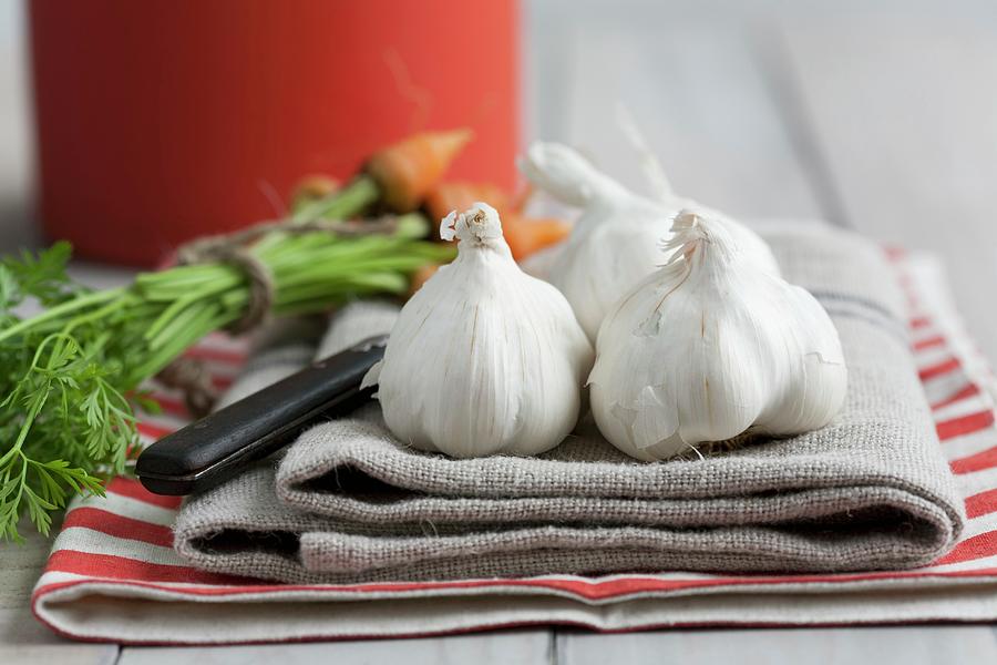 Garlic Bulbs And Baby Carrots On A Tea Towel Photograph by Schindler, Martina
