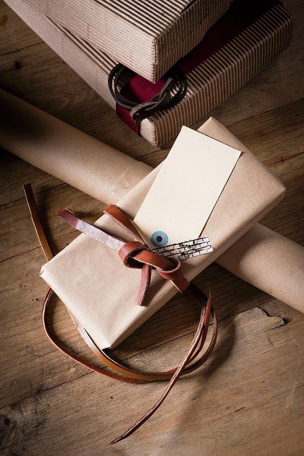 Gift Boxes, Wrapping Paper And Wrapped Presents With Leather Ribbon On Wooden Table Photograph by Great Stock!