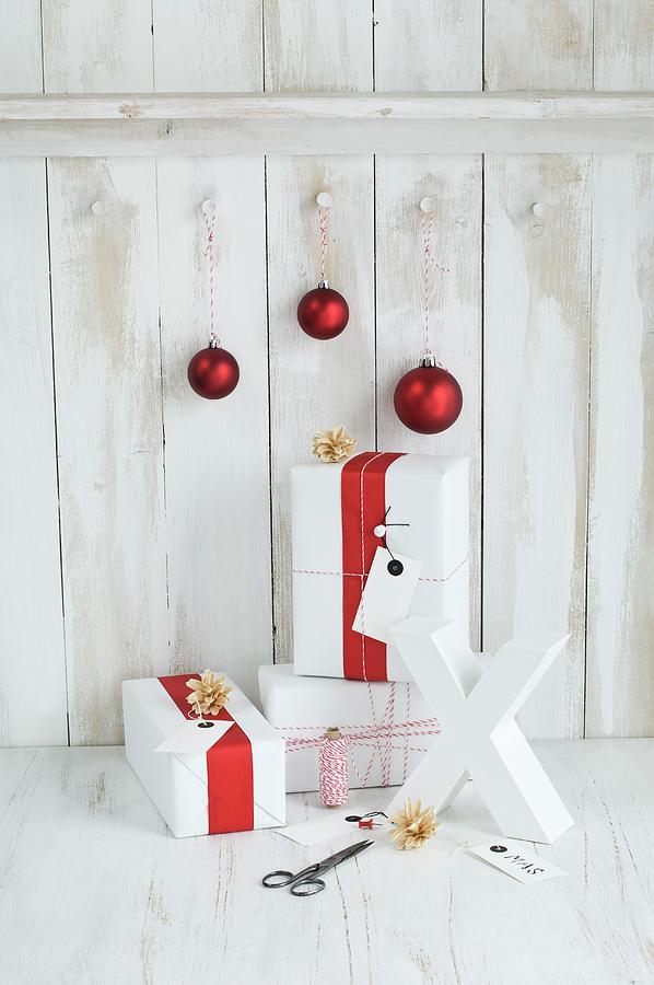 Gifts Wrapped In Red And White, Red Baubles And White X Ornament In Front Of Board Wall Photograph by Achim Sass